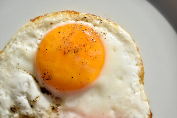 Close up fried egg on plate. Macro egg yolk sprinkled with black pepper