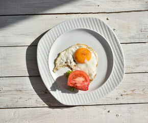Close up fried egg with tomato on plate on wooden background. Top view