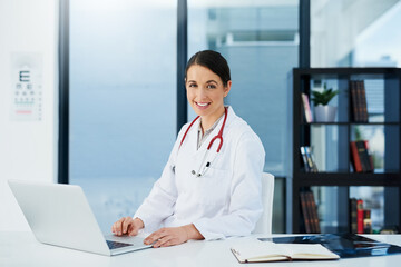 Doctor, woman and portrait at desk with laptop, medical research and planning hospital schedule. Female person, smile and confident for healthcare, cardiologist and clinic website for expert medicare