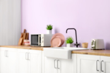 Blurred view of modern kitchen with counters, sink and utensils near pink wall