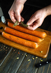 Homemade sausages on the kitchen board. The chef hands add rosemary to the sausage before preparing dinner.