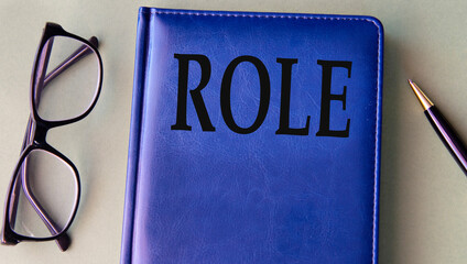 ROLE - word on blue notebook on grey background with pen and glasses