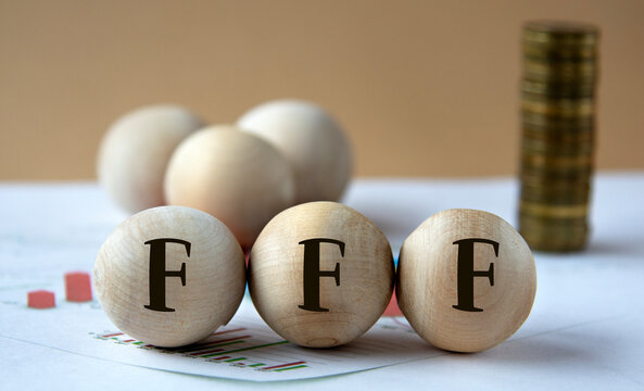 FFF - abbreviation on wooden balls on a background of coins and graphics.