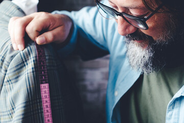 Tailor man at work taking measures on garment in the workshop. Alternative job. People in handmade working activity. Side view of professional worker working happy alone. Fashion industry concept