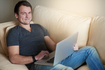 Man, portrait and smile on sofa with laptop for relax, research and reading in living room of home. Person, computer and happy for communication, networking on internet and streaming on couch