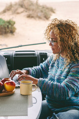 One modern female tourist working on laptop sitting inside a modern camper van with beach view...