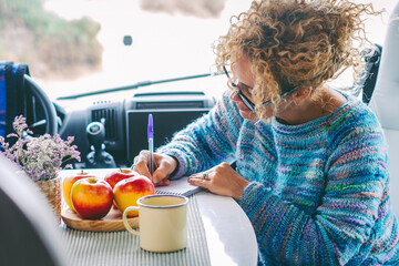 Travel vanlife lifestyle people concept. One woman having breakfast and writing road trip maps sitting inside the cabin of a modern camper van motorhome alone. Lady traveler and freedom concept
