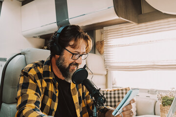 One modern traveler young adult man speaking at the microphone in podcast recording business activity. Digital nomad and smart working inside a camper van. People at work in alternative office desk