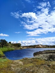 Landscape photo of a small lake formed on the Dutch dunes after rain, with clouds in the background