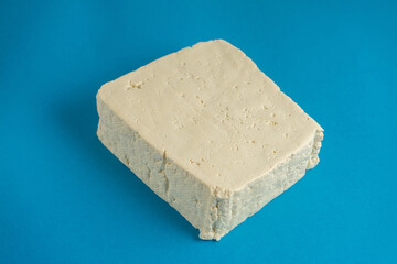 A block of white tofu sits against a bright blue background, its smooth texture and clean edges...