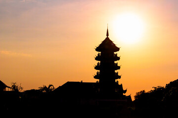 Black silhouette of Pagoda of Che Chin Khor Temple against orange dusk sky at Bangkok, Thailand....