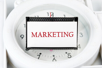 A word MARKETING on a business card on a stand on a lying watch - Powered by Adobe