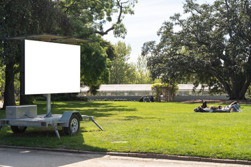 Mockup background texture of a solar powered LED Message Display Board mounted on a trailer or an electronic traffic notice sign, displayed outdoor on grass lawn in a public urban park with people.