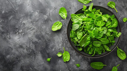 A bowl of green spinach leaves on a grey background. The spinach leaves are scattered around the bowl, creating a sense of abundance and freshness