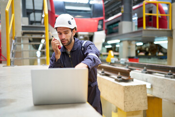 worker working on laptop computer and talking on walkie talkie at construction train station