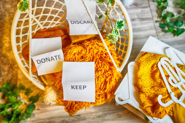 Signs with the words keep, donate, discard and fashion clothes folded in stacks in cozy room. The concept of cluttering, decluttering. Background
