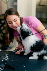 in a grooming salon a young girl groomer in a pink T-shirt kisses a white-black dog