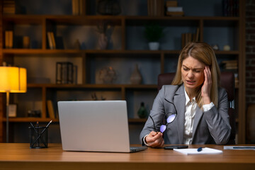 Businesswoman sitting alone in her home office and suffering from a headache. Young businesswoman experiencing fatigue during her work day at home.
