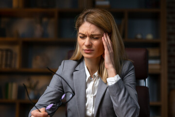 Businesswoman sitting alone in her home office and suffering from a headache. Young businesswoman experiencing fatigue during her work day at home.