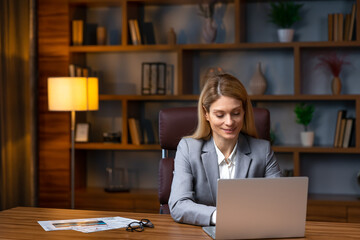Cheerful business lady working on laptop in office, happy beautiful businesswoman in formal suit work in workplace. Attractive female employee office worker smile.