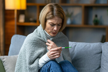 Adult woman is looking at the thermometer. She has fever.