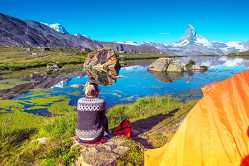 A young girl near tent looks at a fantastic mountain landscape with Matterhorn in the Swiss Alps,...