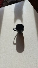 A cup of coffee on a table and long shadows of a cat and a cup, flat lay, copy space
