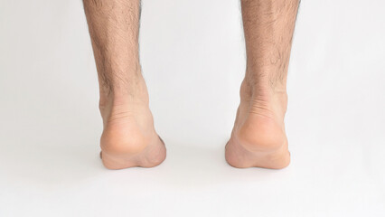 Male feet standing on tiptoe viewed from behind at the Achilles heel, with white background and space for text