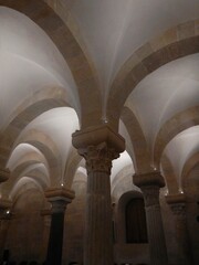 Multiple arches form a vaulted ceiling of an old crypt. Large stone blocks form the walls and arches. The pillars are mismatched.