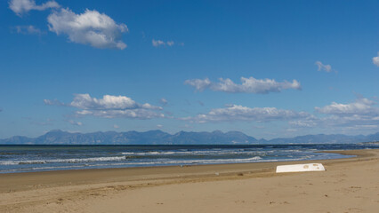 Sandy sea beach with white boat and Amalfi Coast in the background on a sunny day, Paestum, Campania, Italy