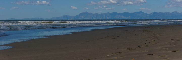 Panorama of sandy sea beach with Amalfi Coast in the background on a sunny day, Paestum, Campania, Italy