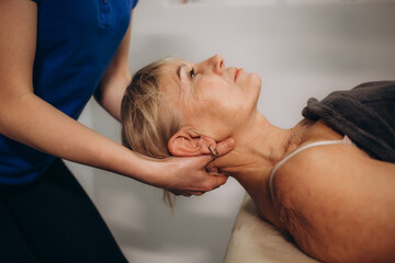 a rehabilitator massages the neck of an elderly woman