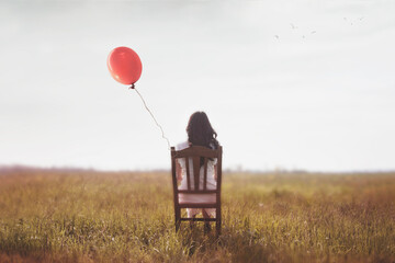 woman sitting from behind in the middle of a field with a red balloon, abstract concept