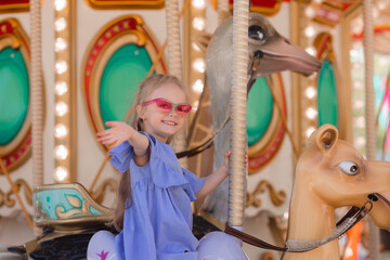 A happy little girl rides a carousel in the summer at an amusement park