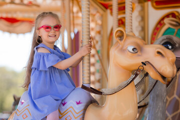 A happy little girl rides a carousel in the summer at an amusement park