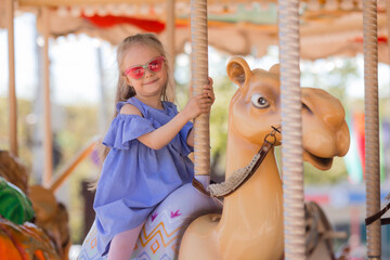 A happy little girl rides a carousel in the summer at an amusement park