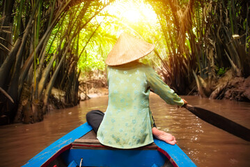 Woman with asian hat rowing a boat by coconut palm trees at Mekong delta