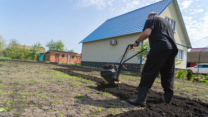 The cultivator processes the chernozem. Farmer cultivating a plot of land before planting vegetables. Summer cottage work in May. Work on the summer cottage for the May holidays.