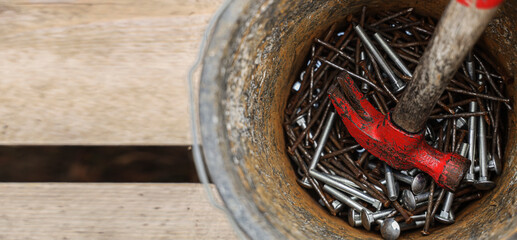 steel nail construction tool in rusty iron bucket. High angle view of various equipment in bucket on wooden boards floor. top view. Old rust nails ans screws are collected in a small bucket.