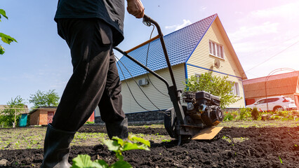 A summer cottage and a man with a small tractor cultivator develops land, on the background of a...