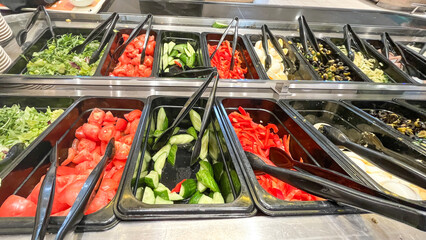a close-up of a salad bar with vibrant, fresh vegetables. Fresh cucumbers, tomatoes, greens, bell...