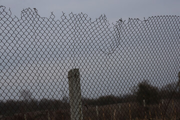 High net fence with barbed wire, concrete pillar, pole, beam against blue grey sky. meadow, field...
