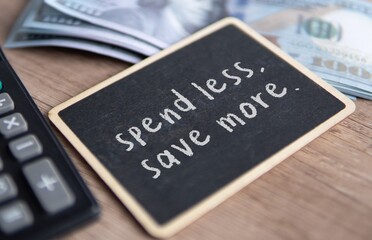 Top view image of chalkboard with text SPEND LESS, SAVE MORE surrounded by money and calculator.