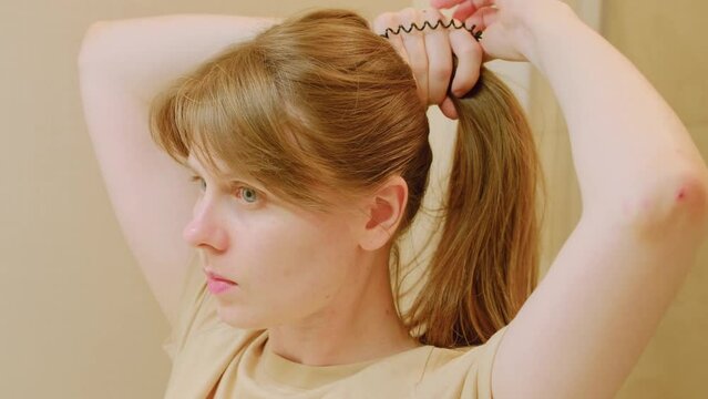 Woman puts her hair in a ponytail in bathroom. Young woman doing her hair in front of a mirror. Daily routine. Woman grab her hairs after wake up. Self care concept