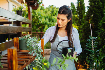 One young caucasian woman is taking care of her plants using plant mister and water can