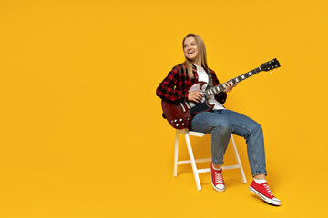Attractive young girl playing the guitar on a yellow background