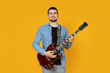 Attractive young guy with a guitar in his hands on a yellow background