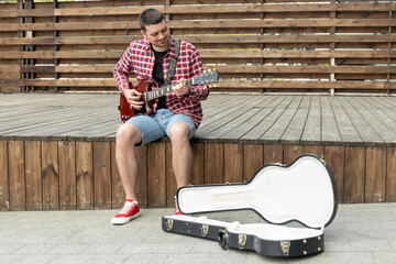 Stylish young guy playing guitar sitting on wooden stage
