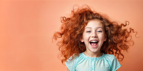 Cute young child  Little girl smiles. Emotion and child development. Little girl smiles while red hair.  A young girl with curly hair is smiling and laughing while wearing a shirt.
