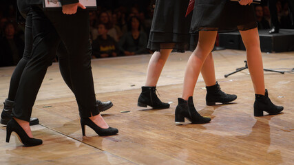 Die Beine, Füße und schwarzen Schuhe von Menschen die auf einer Bühne gehen. 